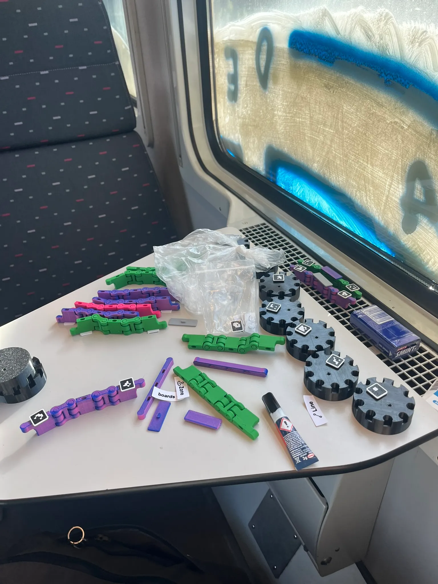 Purple, green and pink ArcUno pieces spread across a fold-down table on a train.