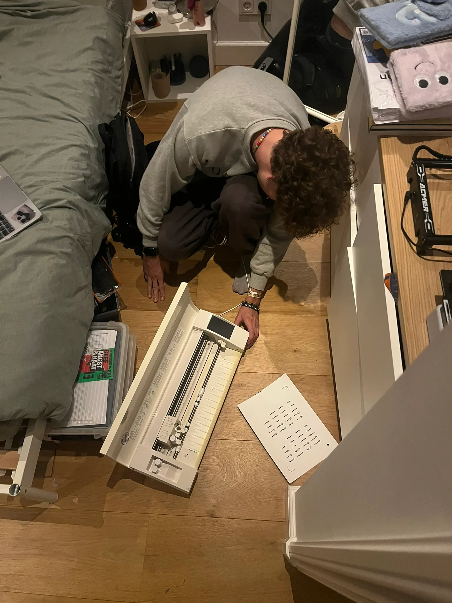 Stijn crouched on the floor beside a small sticker printer and a sheet of labels.