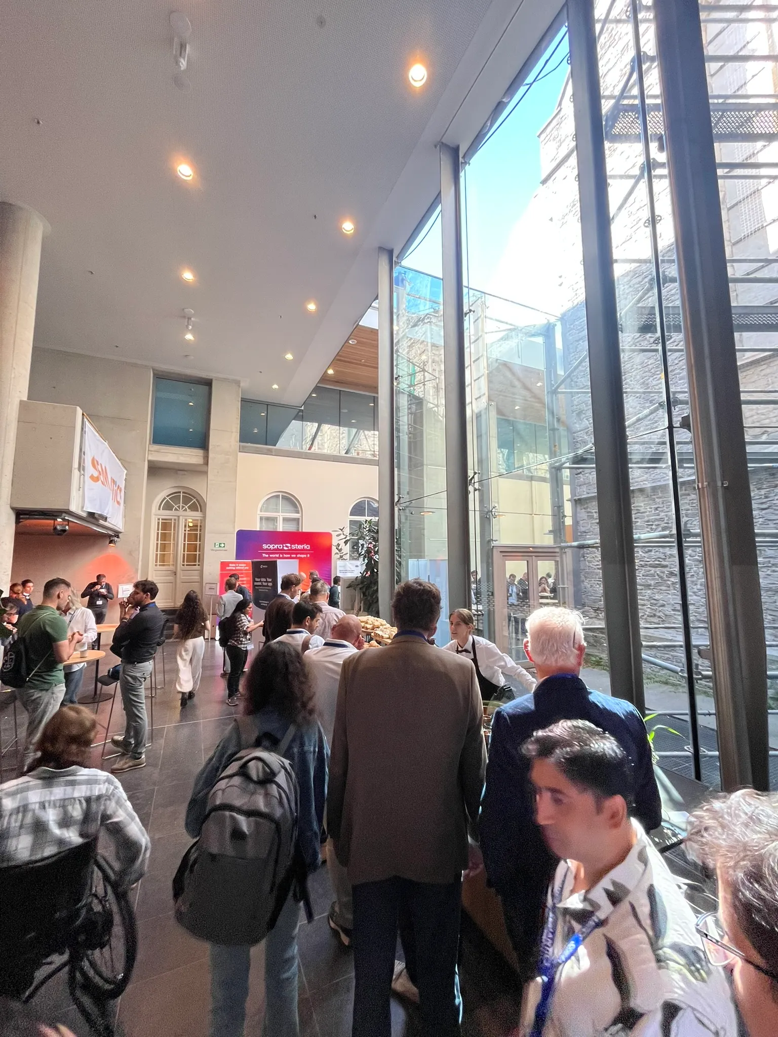 Attendees crowding a bright, glass-walled conference foyer.